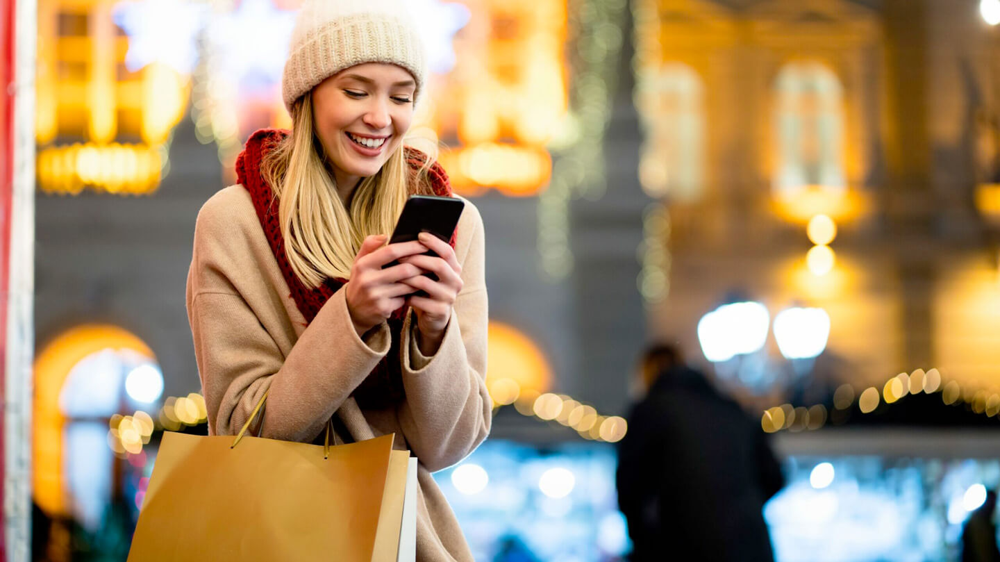 Donna che guarda il telefono mentre fa acquisti per le festività. Articolo Visibilità locale.